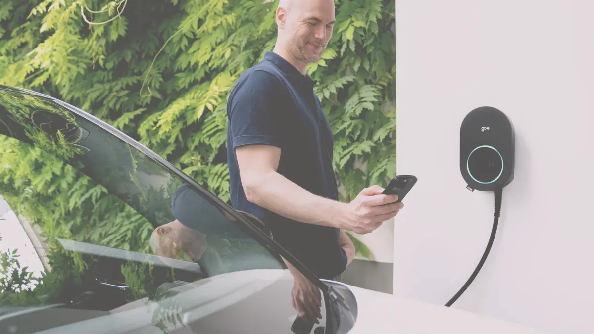 En man vid sin elbil tittar i mobilen bredvid en väggmonterad laddbox